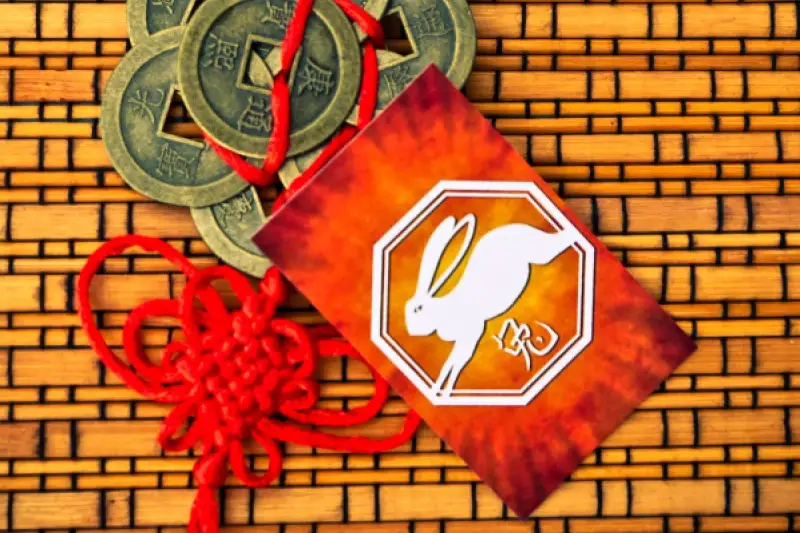 Chiński królik znak zodiaku na tle bambusowym, obok chińskie monety i czerwony węzeł.